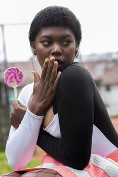 afro woman sitting with a lollipop in her hand and very surprised to see something. High quality photo