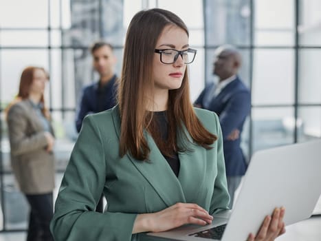 businesswoman or female executive manager in formal suit and eyeglasses, holding laptop and using laptop computer.