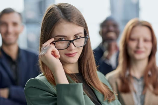 Young executive smiling and standing in a bright room with her team behind her