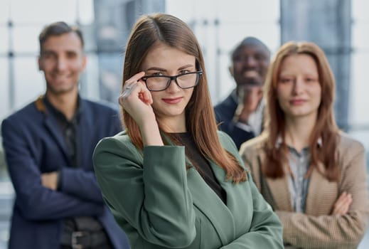 Young executive smiling and standing in a bright room with her team behind her