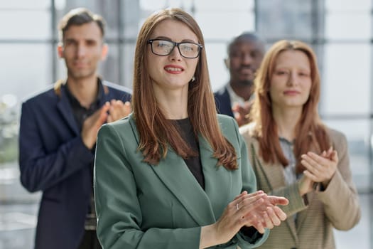 Young executive smiling and standing in a bright room with her team behind her