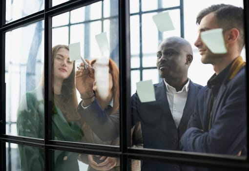 Creative business team looking at sticky notes on glass window