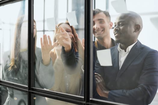 Creative business team looking at sticky notes on glass window
