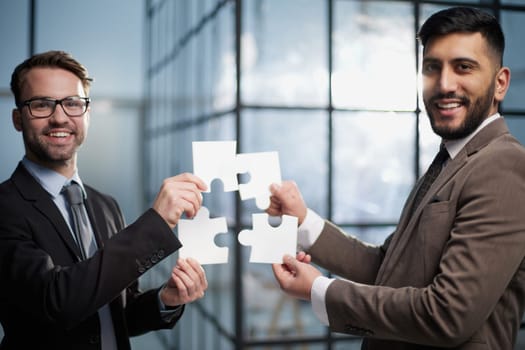 two businessmen put together a puzzle opposite each other on the background of the office