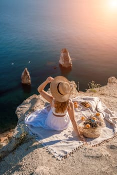 woman sea trevel. photo of a beautiful woman with long blond hair in a pink shirt and denim shorts and a hat having a picnic on a hill overlooking the sea.