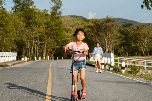 Cute little girl riding scooter on road in outdoor park. Healthy sports and outdoor activities for school children in the summer.