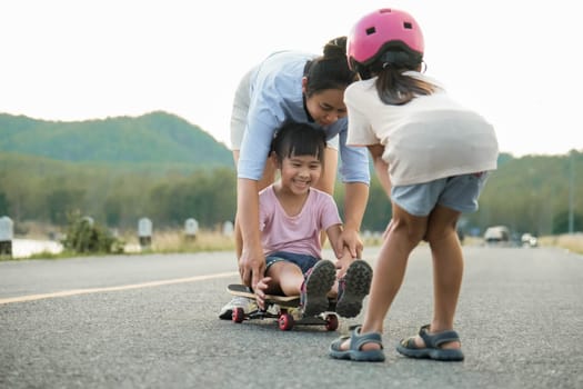 Mother teaching her daughter how to skateboard in the park. Child riding skate board. Healthy sports and outdoor activities for school children in the summer.