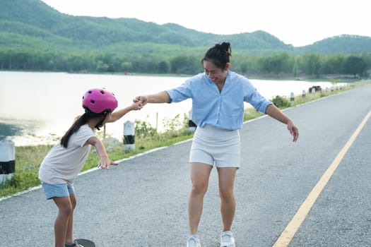 Mother teaching her daughter how to skateboard in the park. Child riding skate board. Healthy sports and outdoor activities for school children in the summer.