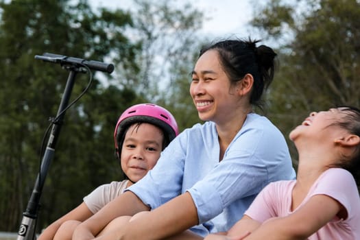 Mother and children sit and rest after riding scooters in the park. Mother and daughters spend their free time riding scooters outdoors together. Happy Loving Family.