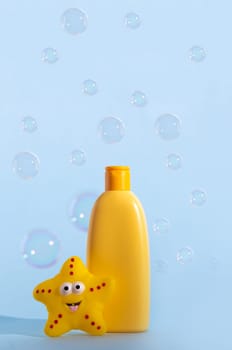 Empty bottle of baby washing gel, bath foam, liquid soap or shampoo with yellow star fish and flying soap bubbles. Children's hygiene. Template for design
