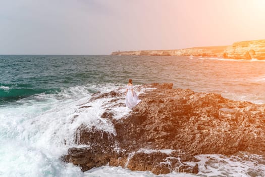 A woman stands on a rock in the sea during a storm. Dressed in a white long dress, the waves break on the rocks and white spray rises