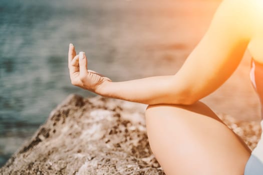 Yoga on the beach. A happy woman meditating in a yoga pose on the beach, surrounded by the ocean and rock mountains, promoting a healthy lifestyle outdoors in nature, and inspiring fitness concept