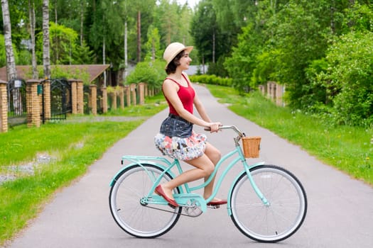 Portrait beautiful young girl in hat with bicycle on street in countryside in sunlight outdoor in a red tank top on a summer day rides on the weekend