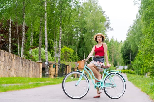 Portrait beautiful young girl in hat with bicycle on street in countryside in sunlight outdoor in a red tank top on a summer day rides on the weekend