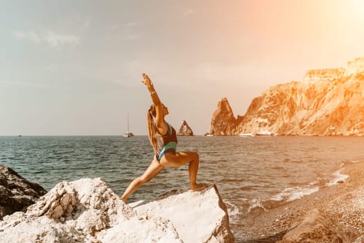 Yoga on the beach. A happy woman meditating in a yoga pose on the beach, surrounded by the ocean and rock mountains, promoting a healthy lifestyle outdoors in nature, and inspiring fitness concept