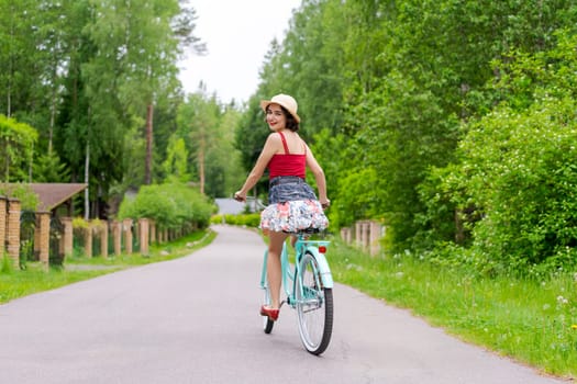 Portrait beautiful young girl in hat with bicycle on street in countryside in sunlight outdoor in a red tank top on a summer day rides on the weekend