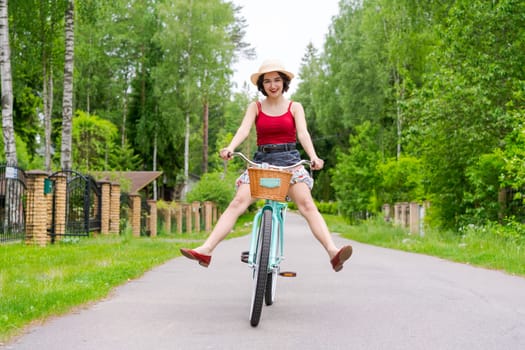 Portrait beautiful young girl in hat with bicycle on street in countryside in sunlight outdoor in a red tank top on a summer day rides on the weekend