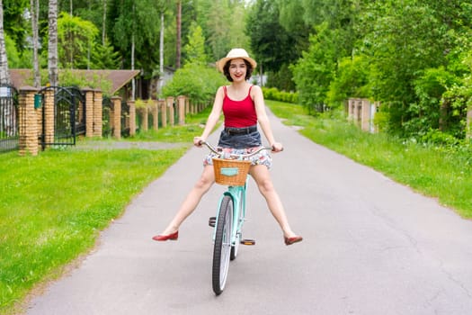 Portrait beautiful young girl in hat with bicycle on street in countryside in sunlight outdoor in a red tank top on a summer day rides on the weekend