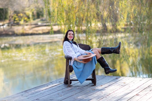 Autumn lake woman. She sits by a pond on a wooden pier in autumn and admires nature. The concept of tourism, weekends outside the city