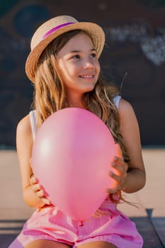 Portrait of a girl in a hat with a pink balloon. She is dressed in pink clothes and her hair is long and loose