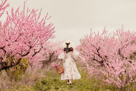 Woman blooming peach orchard. Against the backdrop of a picturesque peach orchard, a woman in a long dress and hat enjoys a peaceful walk in the park, surrounded by the beauty of nature