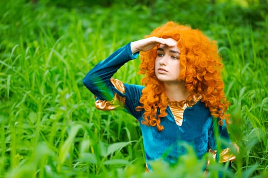 Cute girl in beautiful dress in an forest. Character cosplay festival portrait girl with curly long hair against the background of green bushes in a blue dress