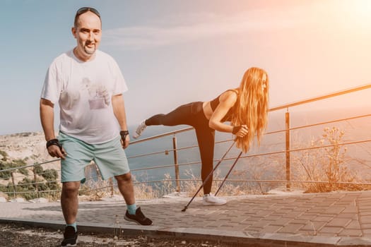 Happy Middle aged couple or friends practicing nordic walking in park near sea. Mature couple with trekking poles walking, practicing Nordic walking outdoors. Aging youthfully and sport concept.