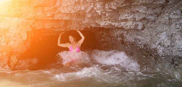 Woman travel sea. Young Happy woman in a long red dress posing on a beach near the sea on background of volcanic rocks, like in Iceland, sharing travel adventure journey