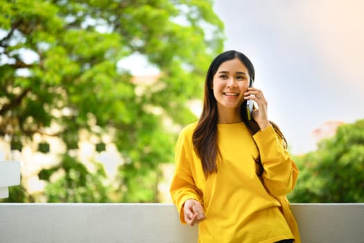 Attractive young woman talking to friends on mobile phone while standing on the balcony of office building.