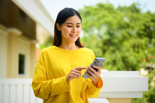 Portrait of smiling asian female student standing outside university building and using smartphone.