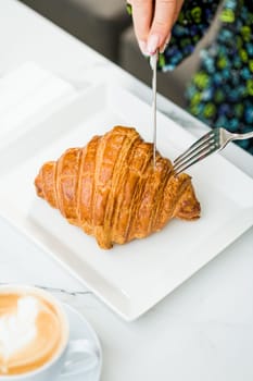 Croissant on a white porcelain plate with coffee on the side