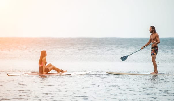 Sea woman and man on sup. Silhouette of happy young woman and man, surfing on SUP board, confident paddling through water surface. Idyllic sunset. Active lifestyle at sea or river