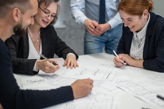 Four colleagues are discussing blueprints in a conference room in an office. Brainstorming of engineers and architects