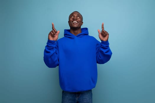 portrait of 30s dark-skinned african man in hoodie pointing with index finger at idea on studio background with copy space.