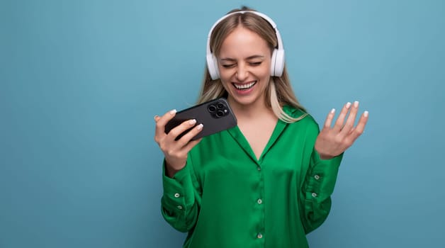 photo of a cute well-groomed young adult woman rejoices listening to music in headphones a song on a blue background.