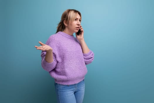 excited blond young woman in purple hoodie talking on the phone on blue background with copy space.