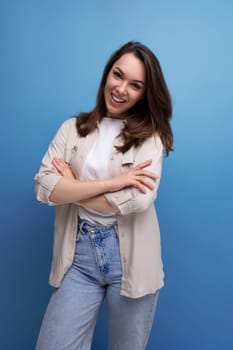 well-groomed smiling brunette 30 year old female person is dressed in a shirt and jeans on a blue background.