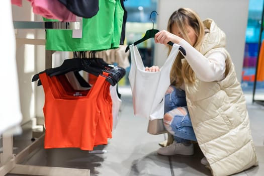 Happy young woman buying new clothes in store. Sale shopping fashion and people concept.