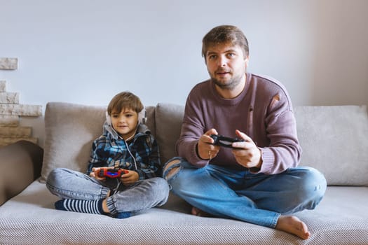 Father And Son Sitting On Sofa In Lounge Playing Video Game.