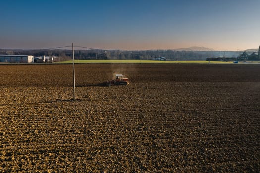 farmer driving a crawler tractor drags a cloud of dust behind, ploughing, power harrowing surface crust breaking to facilitate the birth and seeding of plants on dry soil