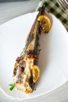 Baked fish with seasonings and spices in a plate on a wooden table