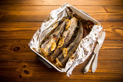 Baked fish with seasonings and spices in foil, in a ceramic form.