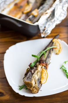 Baked fish with seasonings and spices in a plate on a wooden table