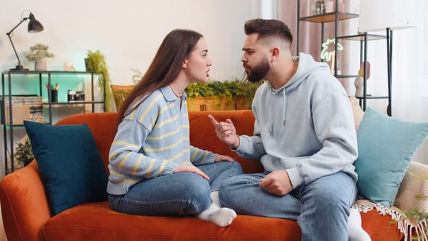 Aggressive family married couple man woman quarreling, shouting at each other at home. Divorce, conflict problem, crisis, distribution of property. Irritated husband and wife on sofa in living room