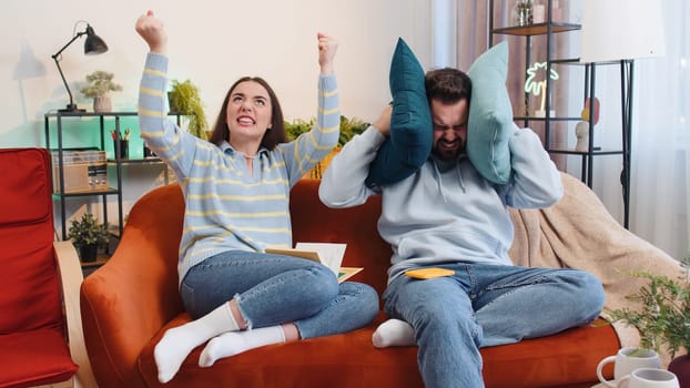 Repair work at neighbours concept. Irritated tired family couple man woman cover ears with pillows annoyed by noisy neighbors suffer from headache wishes silence at home flat without sound insulation