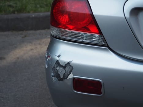Backside of car get scratched, damaged by accident on parking. Abrasions and dents on the rear bumper of silver car after a slight collision accident.