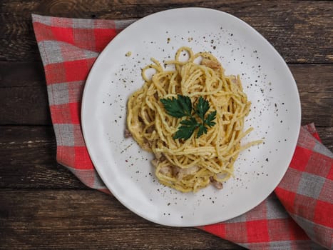 Classic homemade pasta carbonara. Spaghetti with bacon, egg yolk and parmesan cheese on light plate on dark wooden background. Traditional italian cuisine. Top view with copy space.