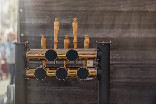 Pouring beer in a bar, mockup for inserting your advertisement. Bronze shiny tap for pouring craft beer on a wooden background, with copy space. High quality photo
