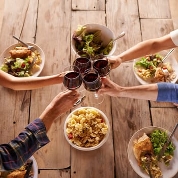 Hands, toast with wine glasses and food with cheer for celebration at lunch. Top view of event, congratulations or success and friends or family sharing a meal or dish together at table with drinks.