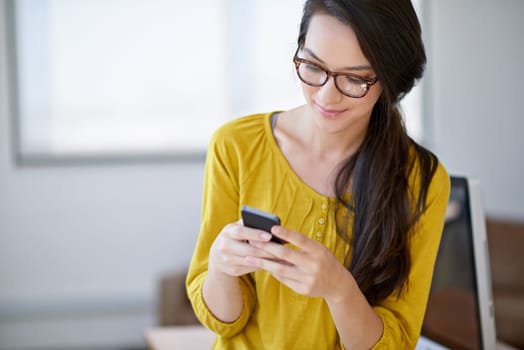 Communication is important in any workplace. an attractive young woman using a cellphone in an office
